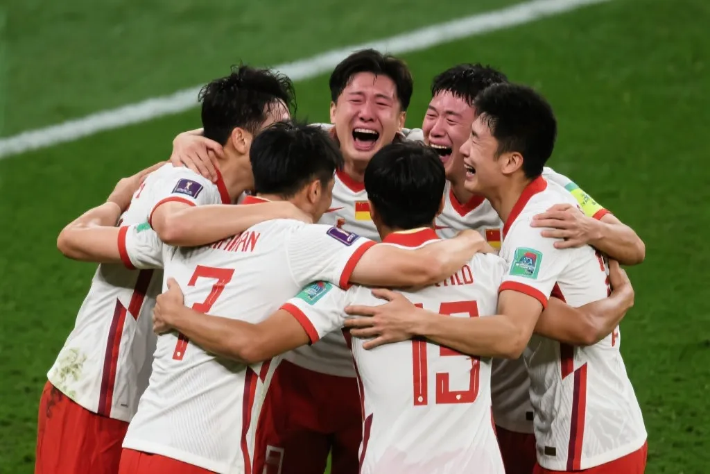 一群身穿国家队战袍的球员在绿茵场上紧紧拥抱，脸上洋溢着激动的泪水与笑容，展现无与伦比的团队凝聚力